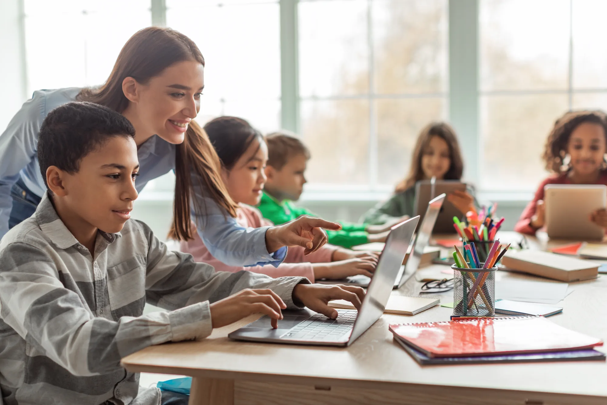A teacher helping students on laptops in a classroom